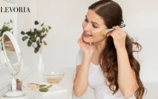 A woman applying a clay facial mask using a cosmetic brush in front of a mirror as part of a daily skincare routine.
