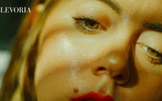 An extreme close-up of a woman's face under dramatic lighting, showing excess shine across her cheeks, nose, and forehead.