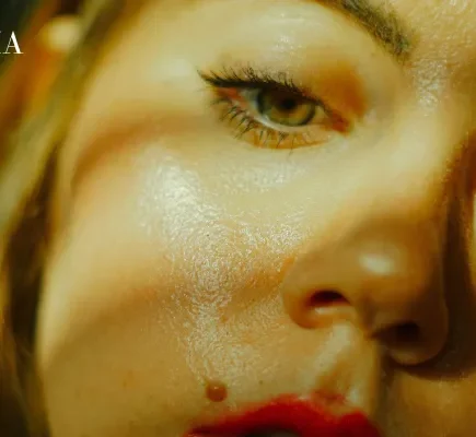 An extreme close-up of a woman's face under dramatic lighting, showing excess shine across her cheeks, nose, and forehead.