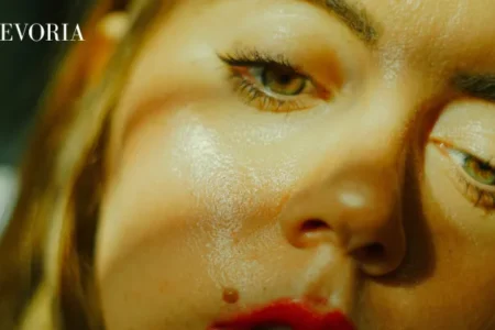 An extreme close-up of a woman's face under dramatic lighting, showing excess shine across her cheeks, nose, and forehead.
