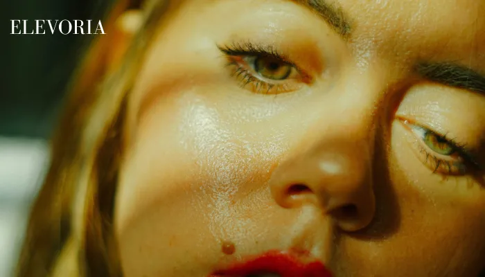 An extreme close-up of a woman's face under dramatic lighting, showing excess shine across her cheeks, nose, and forehead.
