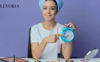 A woman wrapped in a blue hair towel holding a blue alarm clock to emphasize the timing and consistency of skincare routines.