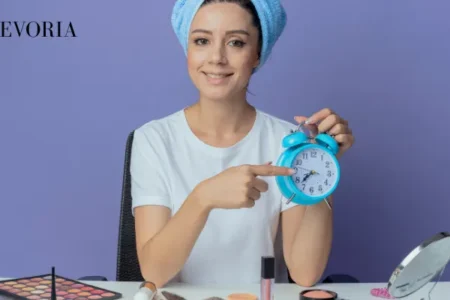 A woman wrapped in a blue hair towel holding a blue alarm clock to emphasize the timing and consistency of skincare routines.