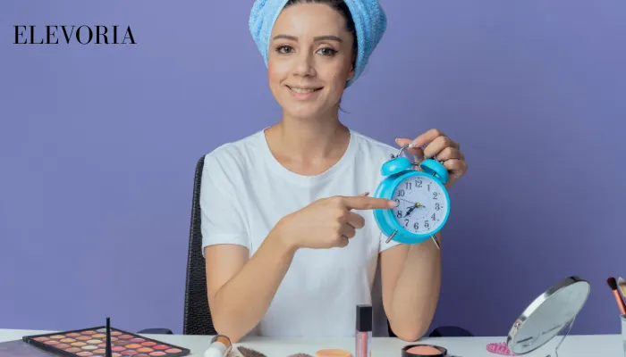 A woman wrapped in a blue hair towel holding a blue alarm clock to emphasize the timing and consistency of skincare routines.